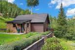 Nestled amidst lush greenery and mature trees, this charming stone and wood cabin offers a serene mountain retreat.