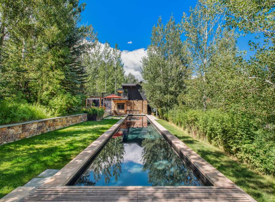 Experience luxury living with this stunning property featuring a sleek, rectangular swimming pool that reflects the vibrant blue sky and lush greenery.