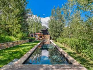 Experience luxury living with this stunning property featuring a sleek, rectangular swimming pool that reflects the vibrant blue sky and lush greenery.