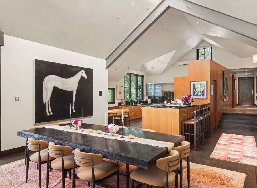 This spacious dining and kitchen area features a large, dark wood dining table set for a gathering, complemented by a striking black and white horse painting.