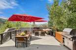 Enjoy al fresco dining and entertaining on this expansive deck, featuring a large wooden dining table with chairs and two vibrant red umbrellas for shade.