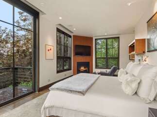 Experience luxury living in this stunning bedroom featuring a cozy fireplace and expansive windows that offer breathtaking views of the surrounding nature.