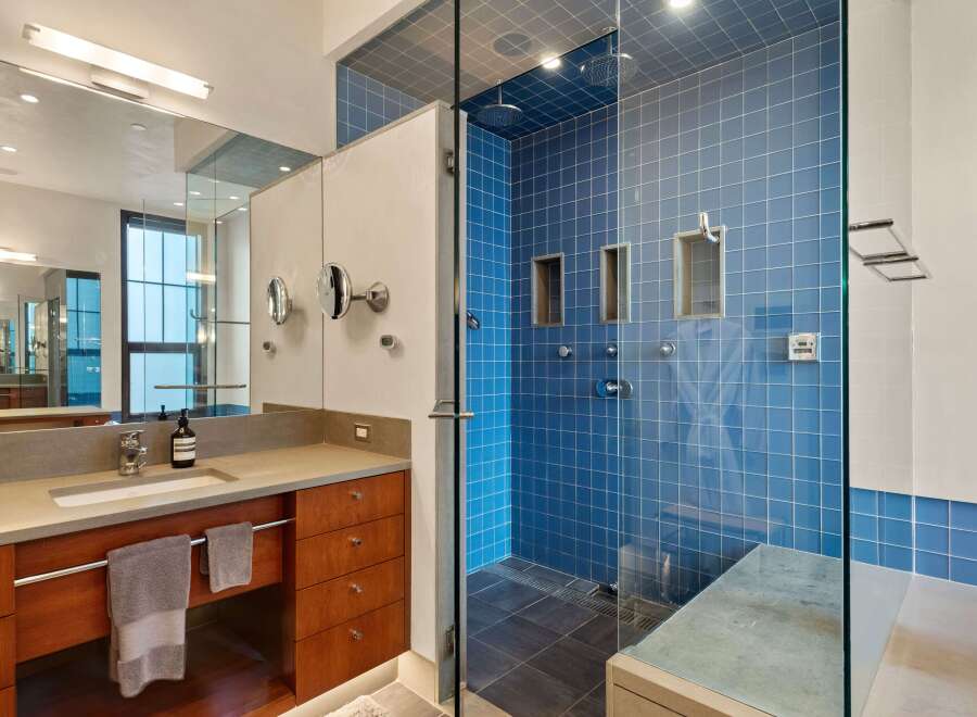 Experience modern luxury in this stunning bathroom featuring a spacious walk-in shower with vibrant blue tilework and multiple shower heads.
