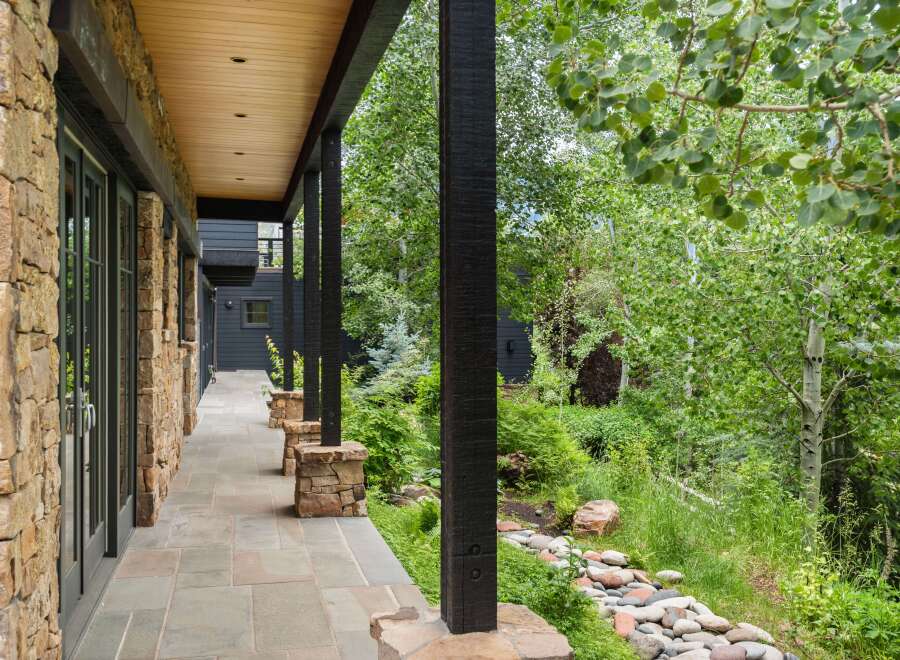 Experience luxurious mountain living with this stunning property featuring a covered stone patio and expansive windows.