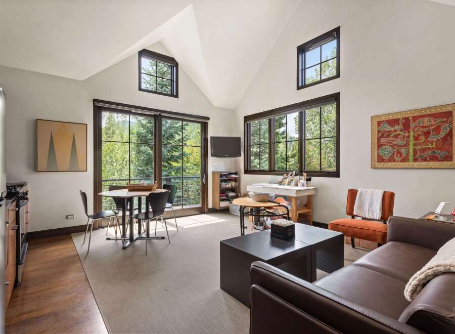 This spacious studio apartment offers a bright and airy living space with large windows framing lush forest views.