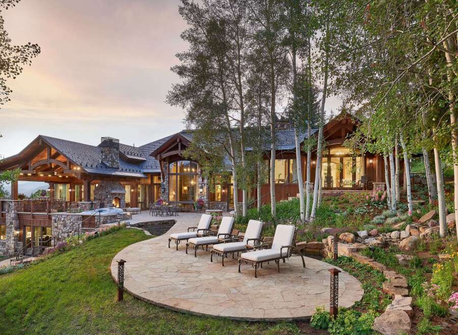 Experience luxury mountain living with this stunning estate featuring a spacious stone patio with chaise lounges, perfect for soaking up the sun.