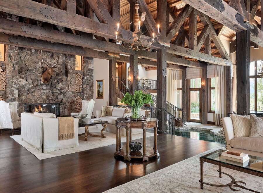 Experience rustic luxury in this grand living room, featuring a massive stone fireplace with a mounted deer head and a cozy wood-burning fire.