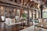 Experience rustic luxury in this grand living room, featuring a massive stone fireplace with a mounted deer head and a cozy wood-burning fire.