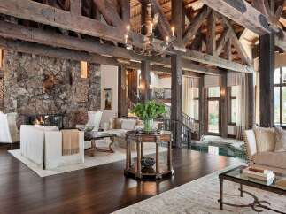 Experience rustic luxury in this grand living room, featuring a massive stone fireplace with a mounted deer head and a cozy wood-burning fire.