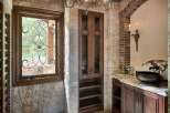 This rustic bathroom features a large stone fireplace, a dark wood vanity with a marble countertop, and a unique vessel sink.