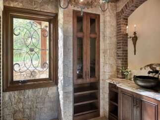 This rustic bathroom features a large stone fireplace, a dark wood vanity with a marble countertop, and a unique vessel sink.