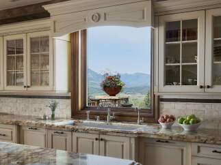 Experience breathtaking mountain views from this stunning kitchen, featuring elegant cream cabinetry and a large window overlooking a picturesque landscape.