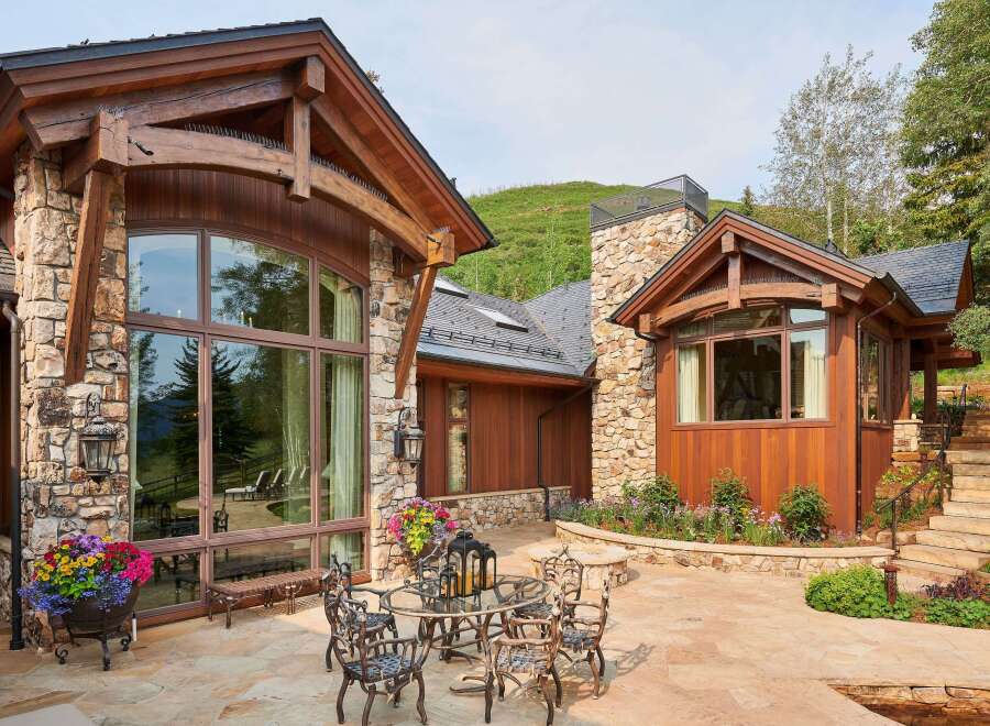 Experience luxury mountain living with this stunning property featuring a rustic stone and wood exterior, expansive windows, and a beautiful stone patio.