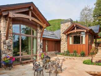 Experience luxury mountain living with this stunning property featuring a rustic stone and wood exterior, expansive windows, and a beautiful stone patio.
