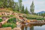 Discover this stunning mountain property featuring a serene tiered water feature cascading into a tranquil pond, surrounded by lush landscaping and natural stone accents.