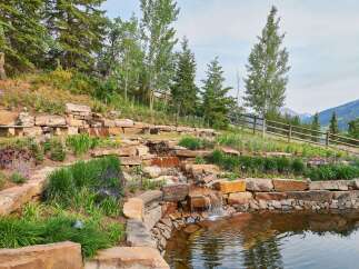Discover this stunning mountain property featuring a serene tiered water feature cascading into a tranquil pond, surrounded by lush landscaping and natural stone accents.