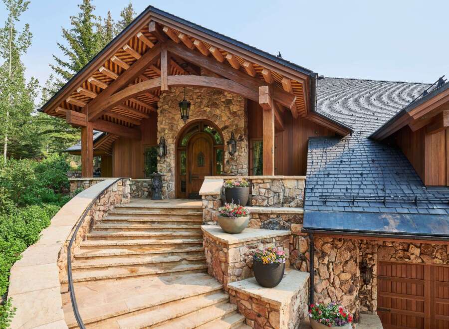 Experience rustic elegance with this stunning mountain home, featuring a grand stone entryway with a charming arched wooden door and exposed timber beams.