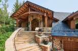 Experience rustic elegance with this stunning mountain home, featuring a grand stone entryway with a charming arched wooden door and exposed timber beams.