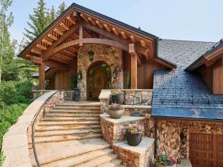 Experience rustic elegance with this stunning mountain home, featuring a grand stone entryway with a charming arched wooden door and exposed timber beams.