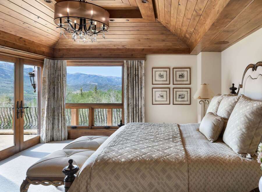 Experience luxury mountain living in this exquisite bedroom featuring a vaulted wood-paneled ceiling and a stunning chandelier.