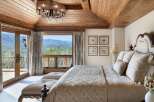 Experience luxury mountain living in this exquisite bedroom featuring a vaulted wood-paneled ceiling and a stunning chandelier.
