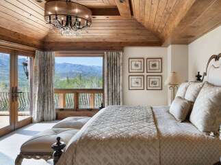Experience luxury mountain living in this exquisite bedroom featuring a vaulted wood-paneled ceiling and a stunning chandelier.