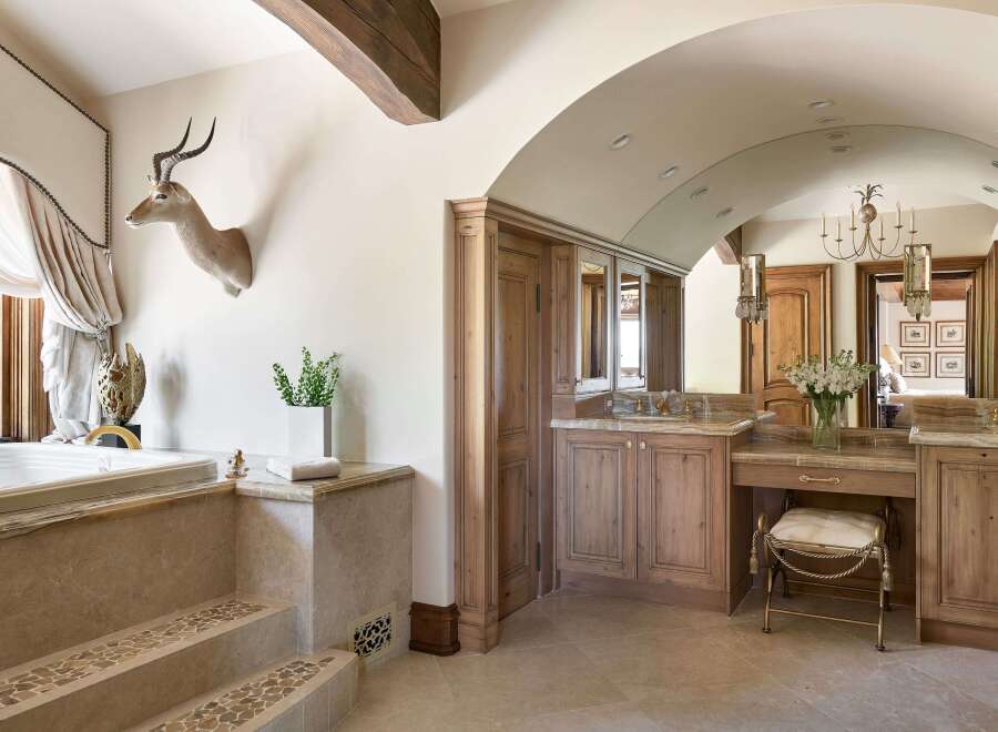 Experience rustic luxury in this stunning bathroom, featuring a deep soaking tub with elegant stone steps and a unique taxidermy antelope mount.