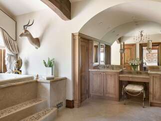 Experience rustic luxury in this stunning bathroom, featuring a deep soaking tub with elegant stone steps and a unique taxidermy antelope mount.