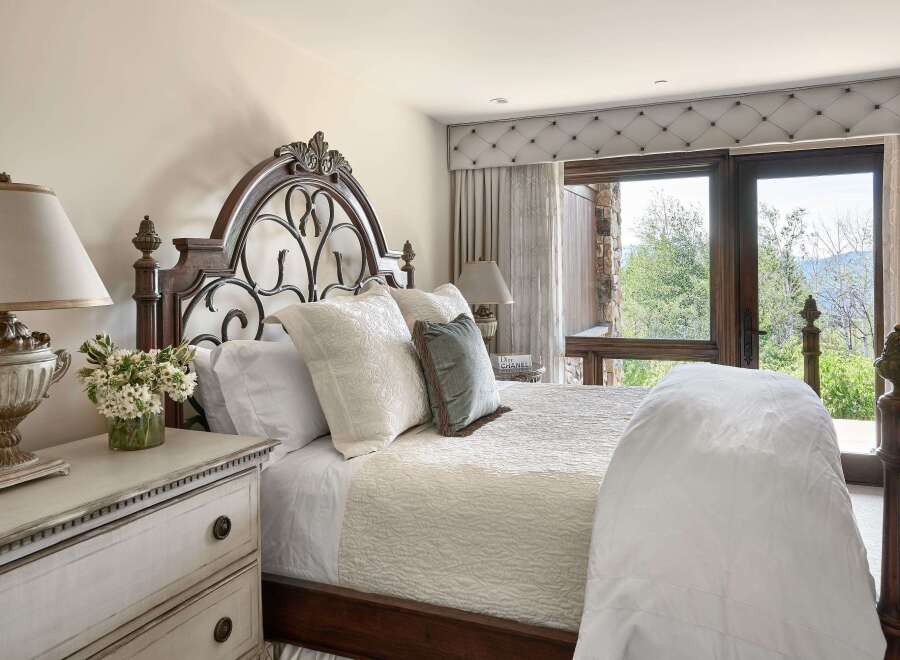 Experience luxury mountain living in this exquisite bedroom, featuring a grand dark wood and wrought iron bed adorned with plush white linens and decorative pillows.