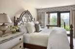 Experience luxury mountain living in this exquisite bedroom, featuring a grand dark wood and wrought iron bed adorned with plush white linens and decorative pillows.