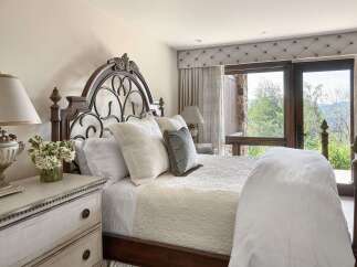 Experience luxury mountain living in this exquisite bedroom, featuring a grand dark wood and wrought iron bed adorned with plush white linens and decorative pillows.