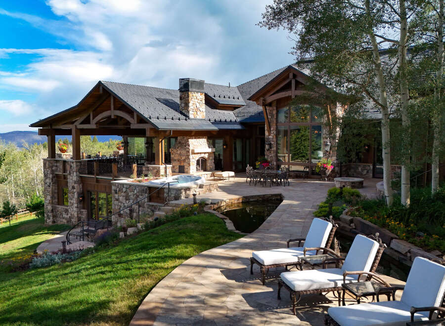 Experience luxury mountain living in this stunning estate, featuring a spacious outdoor living area with a hot tub and a serene water feature.