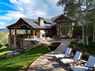 Experience luxury mountain living in this stunning estate, featuring a spacious outdoor living area with a hot tub and a serene water feature.