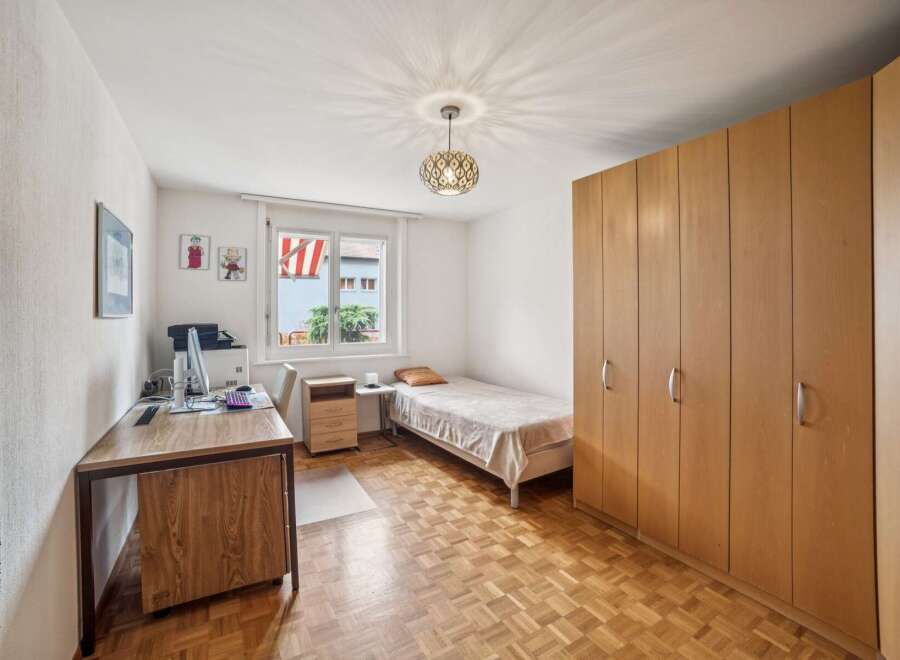 This cozy bedroom features a comfortable single bed, a functional desk with a computer, and ample storage space provided by a large wooden wardrobe.