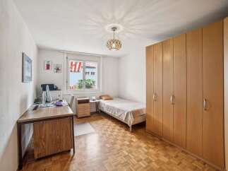 This cozy bedroom features a comfortable single bed, a functional desk with a computer, and ample storage space provided by a large wooden wardrobe.