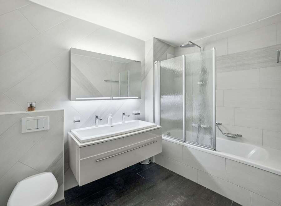 This modern bathroom features a sleek floating vanity with a double sink, illuminated by a stylish mirror with integrated lighting.