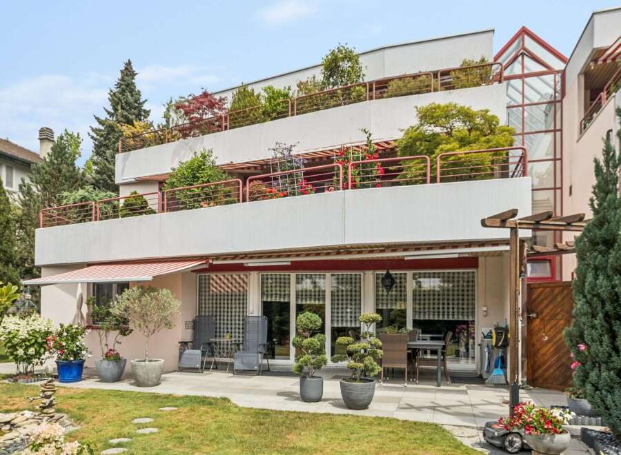 Experience modern living in this multi-level property featuring expansive balconies adorned with lush greenery and vibrant flowers.