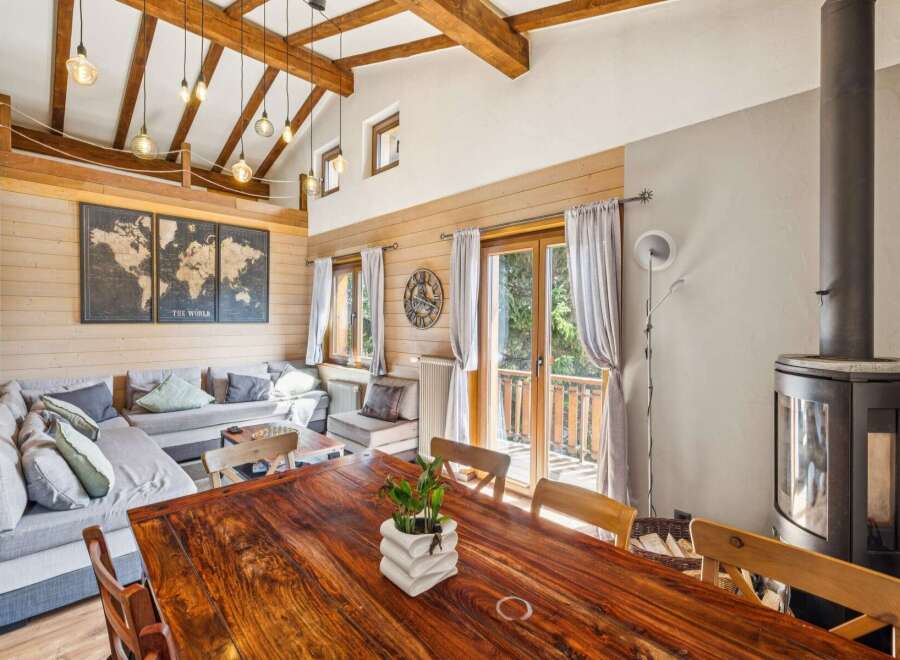 Experience rustic charm in this spacious living and dining area, featuring a large sectional sofa, a stunning wooden dining table, and a cozy wood-burning stove.