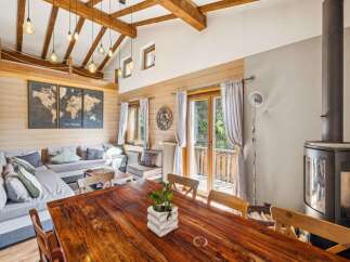 Experience rustic charm in this spacious living and dining area, featuring a large sectional sofa, a stunning wooden dining table, and a cozy wood-burning stove.