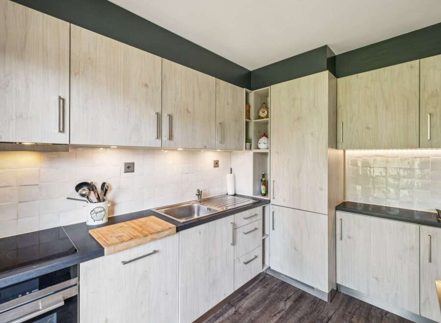 This modern kitchen features light wood cabinetry with sleek silver handles, complemented by a dark countertop and a white tiled backsplash.