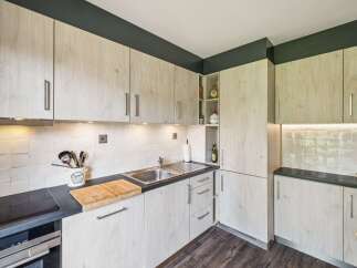 This modern kitchen features light wood cabinetry with sleek silver handles, complemented by a dark countertop and a white tiled backsplash.