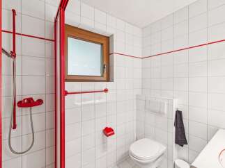 This modern bathroom features a vibrant red shower enclosure and accents, creating a bold contrast with the clean white tiled walls.