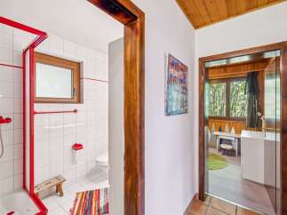 Step into a charming bathroom featuring a vibrant red shower enclosure and white tiled walls, complemented by a wooden window and a colorful striped rug.