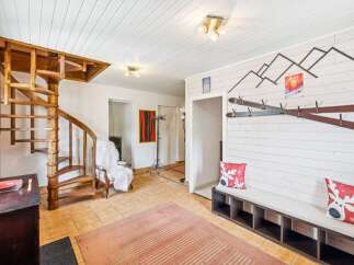 Step into a charming mountain retreat featuring a unique wooden spiral staircase and a cozy seating area with festive holiday pillows.