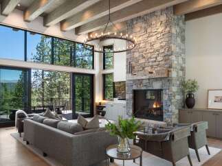 Experience luxury mountain living in this stunning great room, featuring a grand stone fireplace and expansive windows that frame breathtaking forest and mountain views.