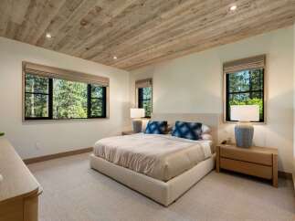 Experience serene living in this beautifully appointed bedroom, featuring a luxurious bed and a rustic wood-planked ceiling.
