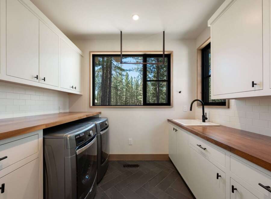 This modern laundry room boasts ample storage with white shaker cabinets and rich walnut countertops.
