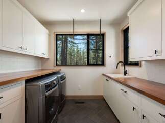 This modern laundry room boasts ample storage with white shaker cabinets and rich walnut countertops.