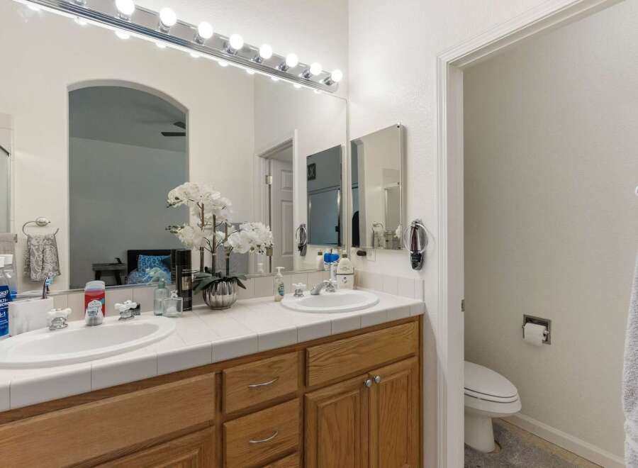 This spacious bathroom features a double vanity with white tile countertops and ample storage space in the light oak cabinets.