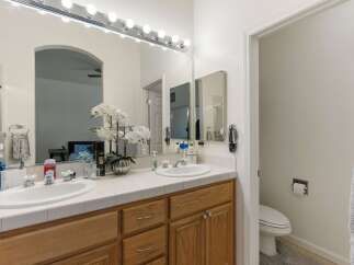 This spacious bathroom features a double vanity with white tile countertops and ample storage space in the light oak cabinets.